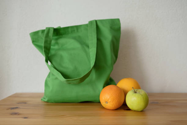 A smiling woman holding a reusable green bag while shopping outdoors in a vibrant market.