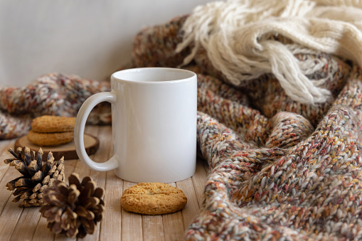 White coffee mug near pine cones, cookies and knitted sweater on wooden table Close up, copy space. winter Christmas mock up. Bohemian, ethnic or scandinavian style