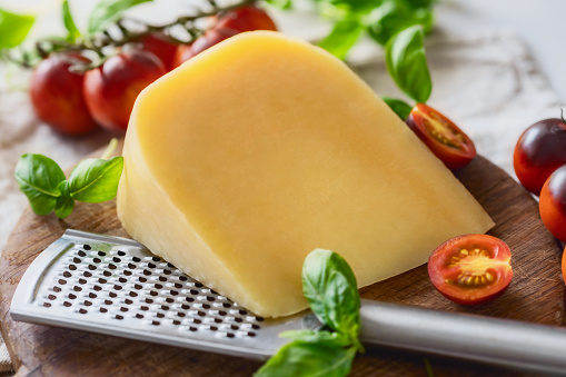 Parmesan cheese with basil leaves, Cherry tomatoes and iron grater on wooden cutting board, cooking background