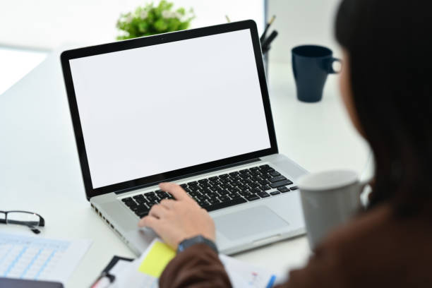 istock Over shoulder view of female office worker drinking coffee and using laptop at workstation 1604885756