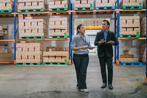 Asian warehouse management having discussion at warehouse with digital tablet