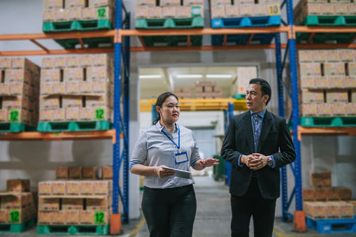 Asian warehouse management having discussion at warehouse with digital tablet