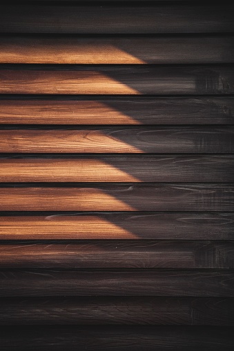A vertical shot of a wooden wall panel illuminated by a stream of golden sunlight.