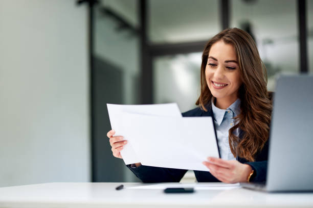 istock A smiling female employee is doing paperwork and using a laptop at the office. 1604910871