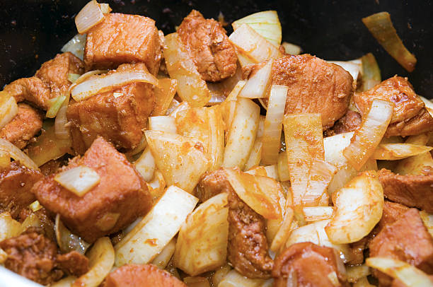 Close up steaming meat cubes with onion pieces and tomato pieces of a goulash dish in black pot