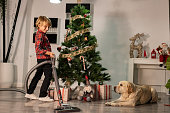 boy cleaning the house vacuuming the living room with the christmas tree with his dog