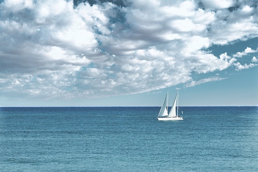 A sailboat sailing on the open sea, with a backdrop of white fluffy clouds in the sky