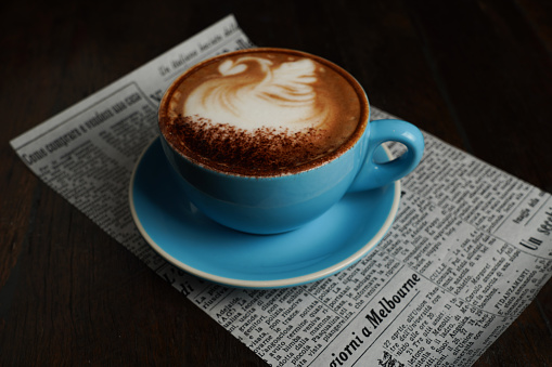 A coffee in a blue cup on a piece of newspaper