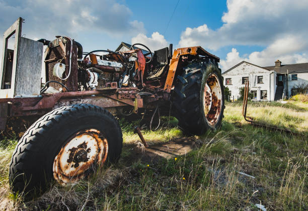 old tractor with missing body parts as rusty engine and mechanical parts are visible. forsaken agricultural vehicle conveys the decline of the cultivation and rural depopulation. cannibalised tractor - inisheer aran islands, county galway, ireland - inisheer imagens e fotografias de stock