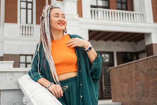 Portrait of a happy young woman with multicolored dreadlocks and a nose piercing on a city street. Hipster woman with trendy pigtails outdoors
