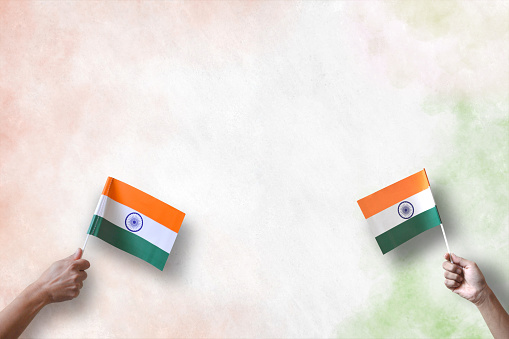 A horizontal photograph of two hands holding tiranga flags of India. A calm peaceful patriotic theme wallpaper. There is no text and Copy space for text. Can be used for national festivals, events, national teams related backdrops like Republic Day, Independence Day celebrations.