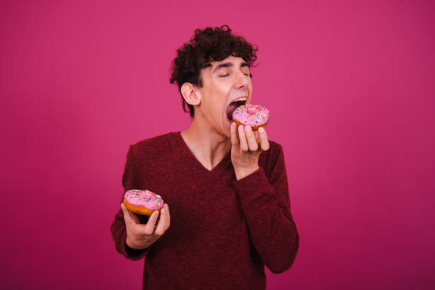 istock Young attractive guy eats pink donuts. Delicious breakfast and good vibes. 1604980541