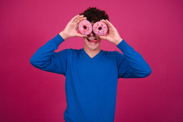 istock Young attractive guy eats pink donuts. Delicious breakfast and good vibes. 1604981623