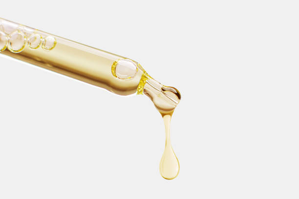 istock Cosmetic pipette with a falling drop of gold color on a light background. 1605016108