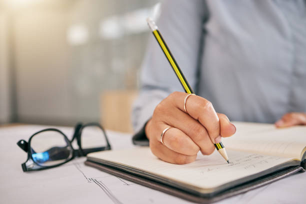 istock Hand, book and a architect woman writing a note in her journal, diary or planner to remember an appointment. Planning, schedule and notebook with a female engineer sitting in her office closeup 1605027931