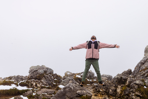 A mid adult man wearing a coat, standing on a rocky mountain while in Garmisch-Partenkirchen, Germany. He has his arms outstretched and is enjoying the fresh around him while looking up with his head back.