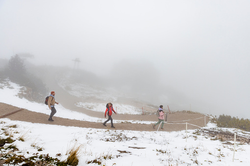 A same sex couple and their friend walking on a footpath down a snowy mountain after getting a cable car up to it while on holiday in Garmisch-Partenkirchen, Germany. They are wearing coats and heading towards the the bottom of the mountain while talking and bonding. The view is low visibility due to the fog.