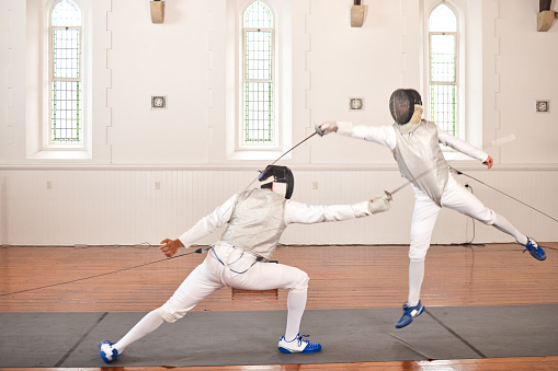 Fencing, sport and people with sword to fight in training, exercise or workout in hall. Martial arts, stab and fencers or men jump in mask and costume for fitness, competition or target in swordplay