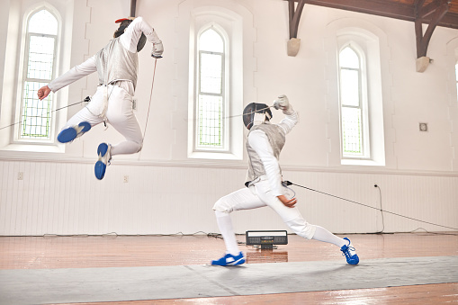 Fencing, jump and sport with sword to fight in training, exercise or workout in a hall. Martial arts, stab and fencers or people with mask and costume for fitness, competition or target in swordplay