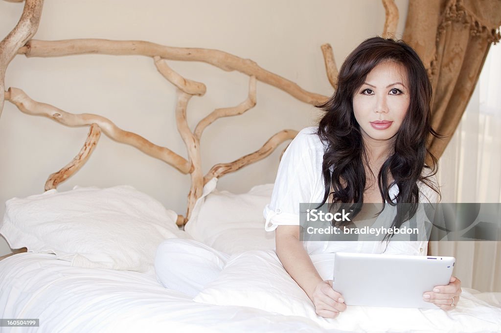 Азиатская женщина, работающих из дома в постели, держа планшет - Стоковые фото Азиатского и индийского происхождения роялти-фри
