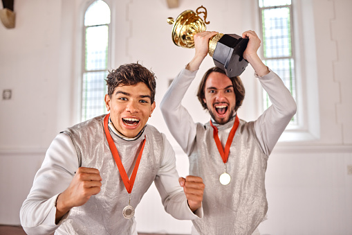 Sports, fencing and portrait of men with trophy for winning competition, challenge and match in gym. Fitness, sword fighting and excited male athletes celebrate with prize for games or tournament