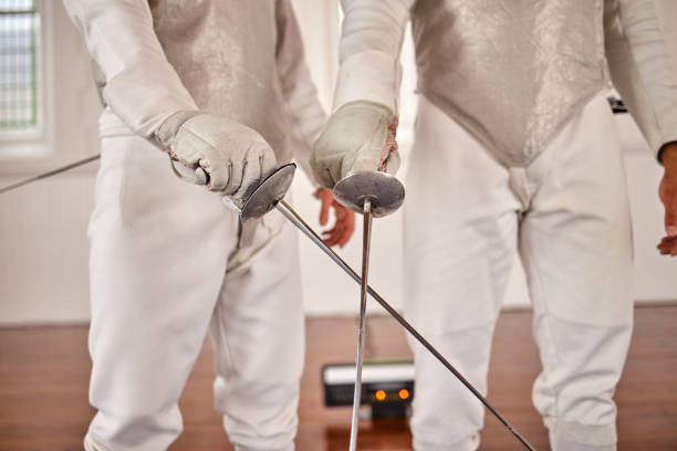 Two fencer in a fencing pose. One is attacking and one is defending. White on black background.