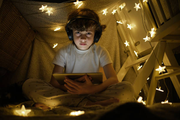 istock Serious boy using tablet and headphones in tent 1605056536