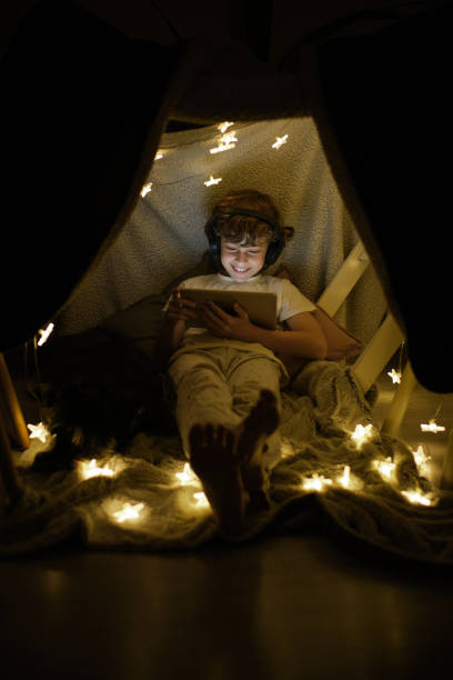 istock Cheerful boy watching video in blanket fort 1605059302