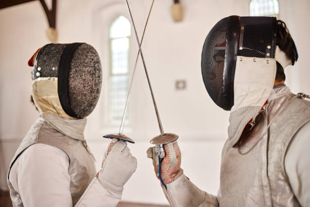 istock Fencing, sport and start fight with sword in training, exercise or challenge in hall. Martial arts, crossed and fencers or people with mask and costume for fitness, competition or target in swordplay 1605059940