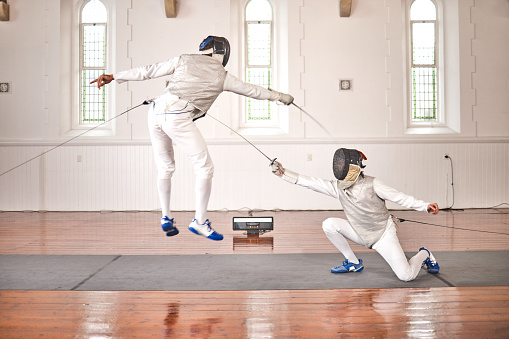 Fencing, sport and jump with sword to fight in training, exercise or workout in a hall. Martial arts, match and fencers or people with mask and costume for fitness, competition or target in swordplay