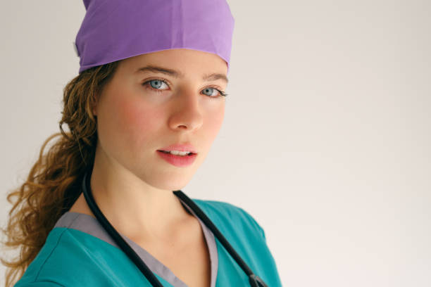 Female Medical Surgical Assistant in scrubs with hair net getting ready for surgery putting on surgical mask