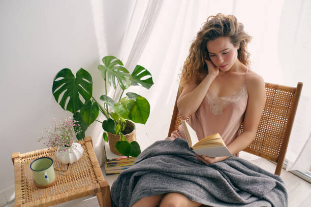 istock Young woman sitting on wicker chair with book 1605081652