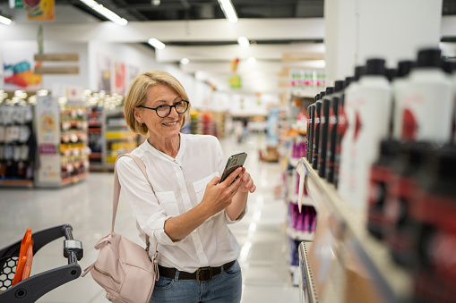Mature woman shopping at the supermarket following a shopping list on her mobile phone