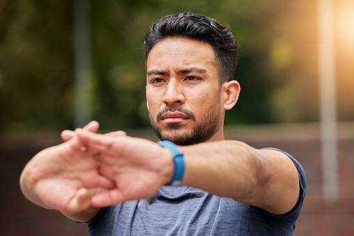 Serious, fitness or man stretching arms in exercise, training or healthy sports outdoor. Face of strong asian athlete focus to warm up in workout, performance or thinking of mobility, energy or power