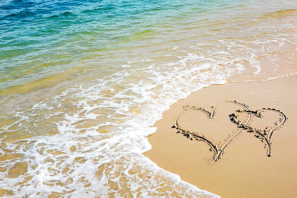 A tropical beach with two hearts drawn into the golden sand stock photo