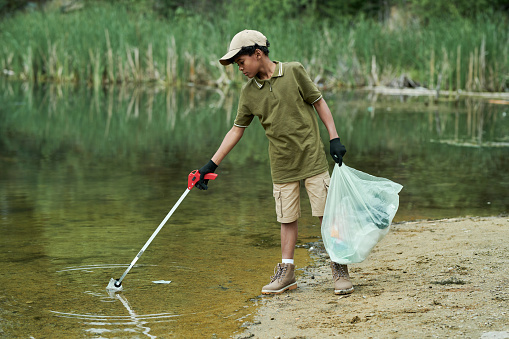 African American boy cleaning the lake from garbage with special stick