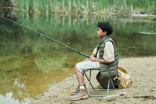 Child sitting on chair with fishing rod and fishing near the lake