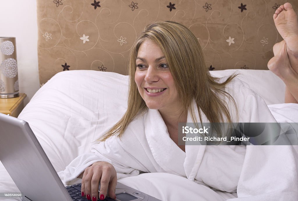 Frau entspannt auf dem Bett mit Laptop - Lizenzfrei Bademantel Stock-Foto