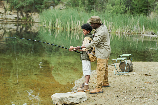 African American dad teaching his son to catch a fish with fishing rod