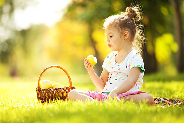 милая маленькая девочка ест яблоко в парке - apple eating little girls green стоковые фото и изображения