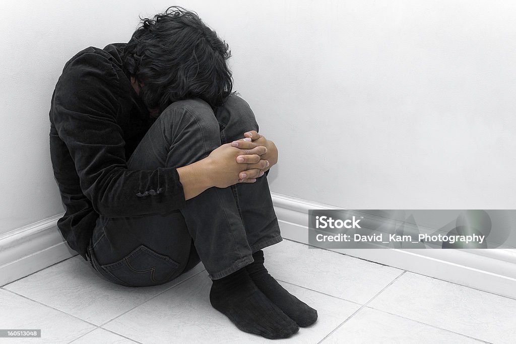 A man in black huddled in a corner Going through harshness. Fetal Position Stock Photo
