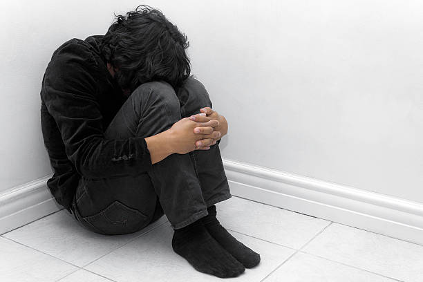 A man in black huddled in a corner Going through harshness. hugging knees stock pictures, royalty-free photos & images