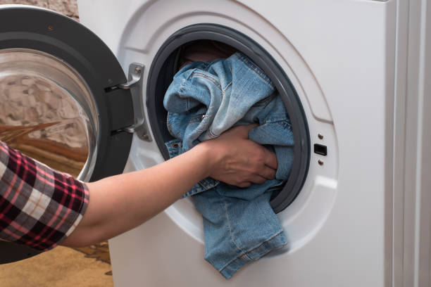 A young girl puts clothes into the washing machine stock photo
