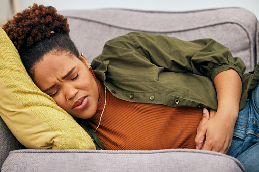 Sick woman, stomach pain and problem on sofa for ibs, health risk or nausea of gastric bloating, period cramps or virus. Black female person, menstruation or stress of constipation from endometriosis