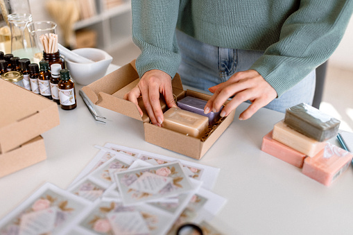 Young entrepreneur woman packing orders for delivery. Woman packing homemade soaps in boxes, getting ready for delivery to the customers.