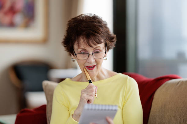 istock Senior woman with pen and notepad at home, looking surprised 1605155544