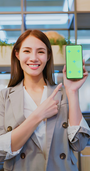 asian happy businesswoman is showing green screen smart phone while standing