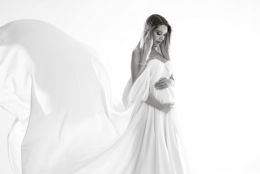 Beautiful Pregnant Woman holding  her Belly wearing white, long Dress. Happy mom to be. A lot of copy space.