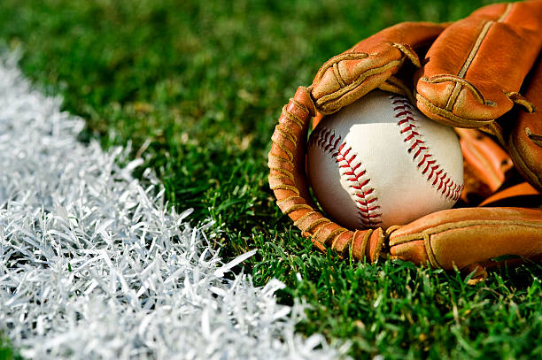 New Baseball in glove along foul line New Baseball inside a baseball glove on the outfield grass next to the foul line baseball stock pictures, royalty-free photos & images