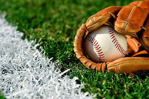 New Baseball inside a baseball glove on the outfield grass next to the foul line